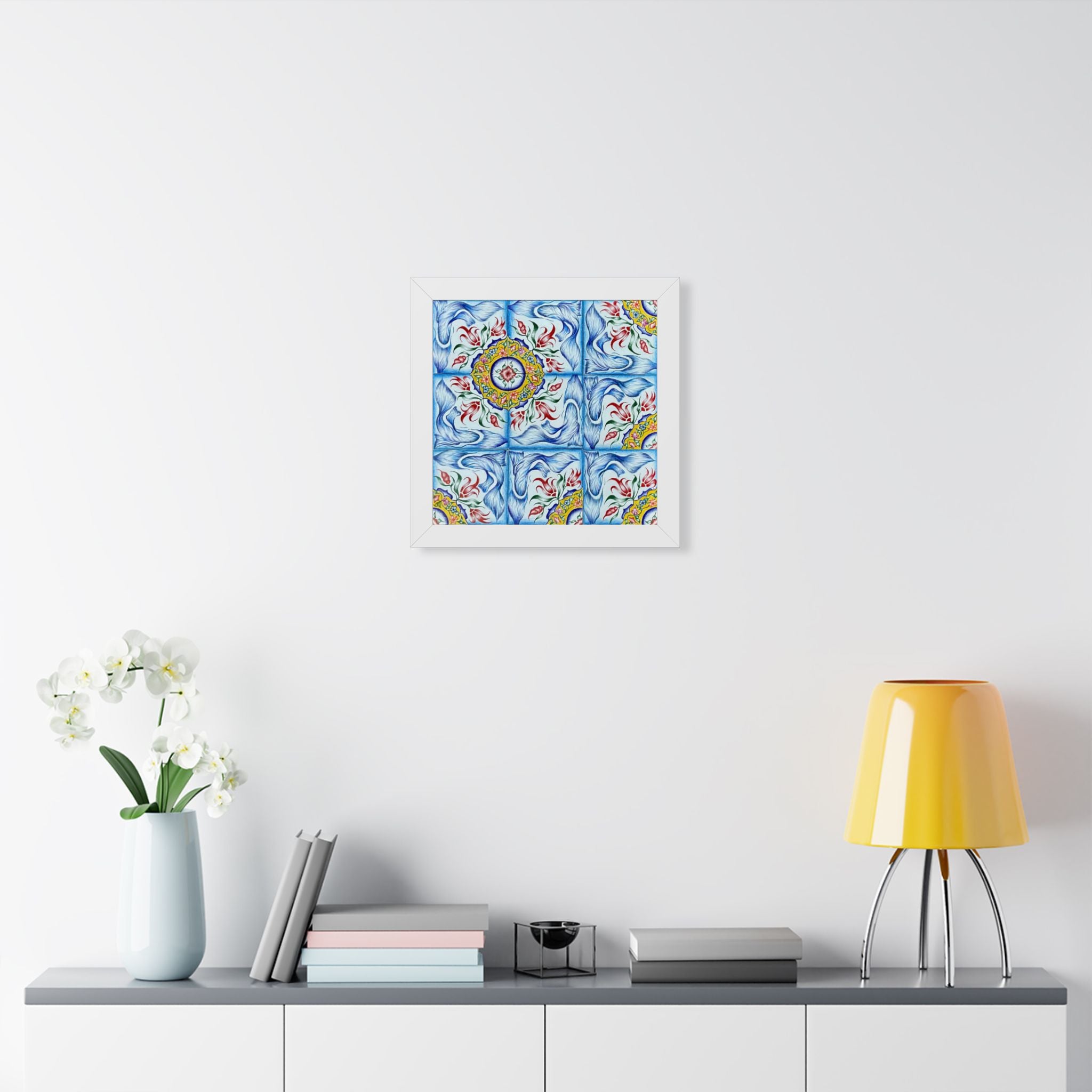 Decorative tile with floral pattern on a wall above a shelf with books and a lamp.